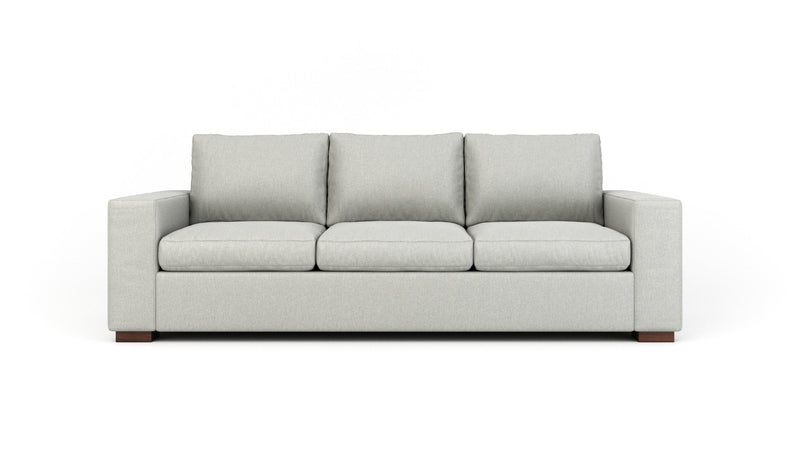 Teal leather ottoman with wooden legs paired with a gray sectional sofa on a patterned rug.