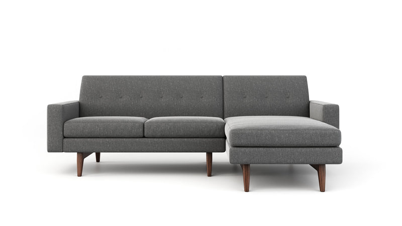 Grey sofa with chaise section in a contemporary living room, featuring a round glass coffee table and matching gray tones.
